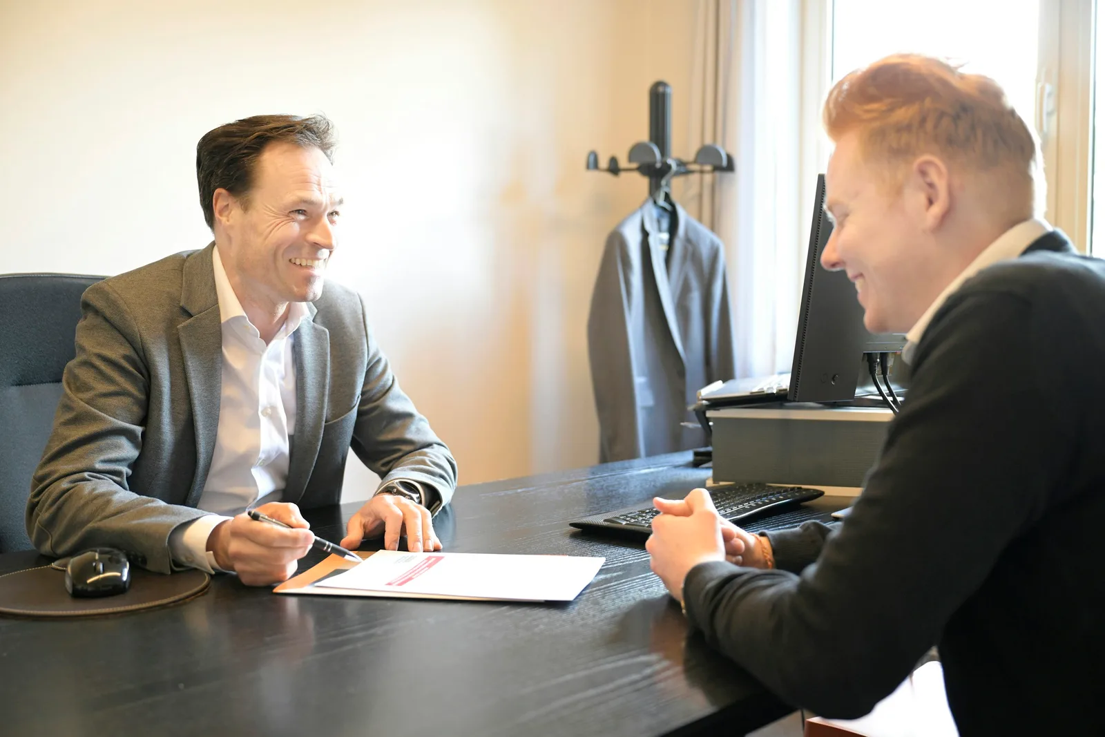 Two professionals in conversation across an office desk, reviewing a document together