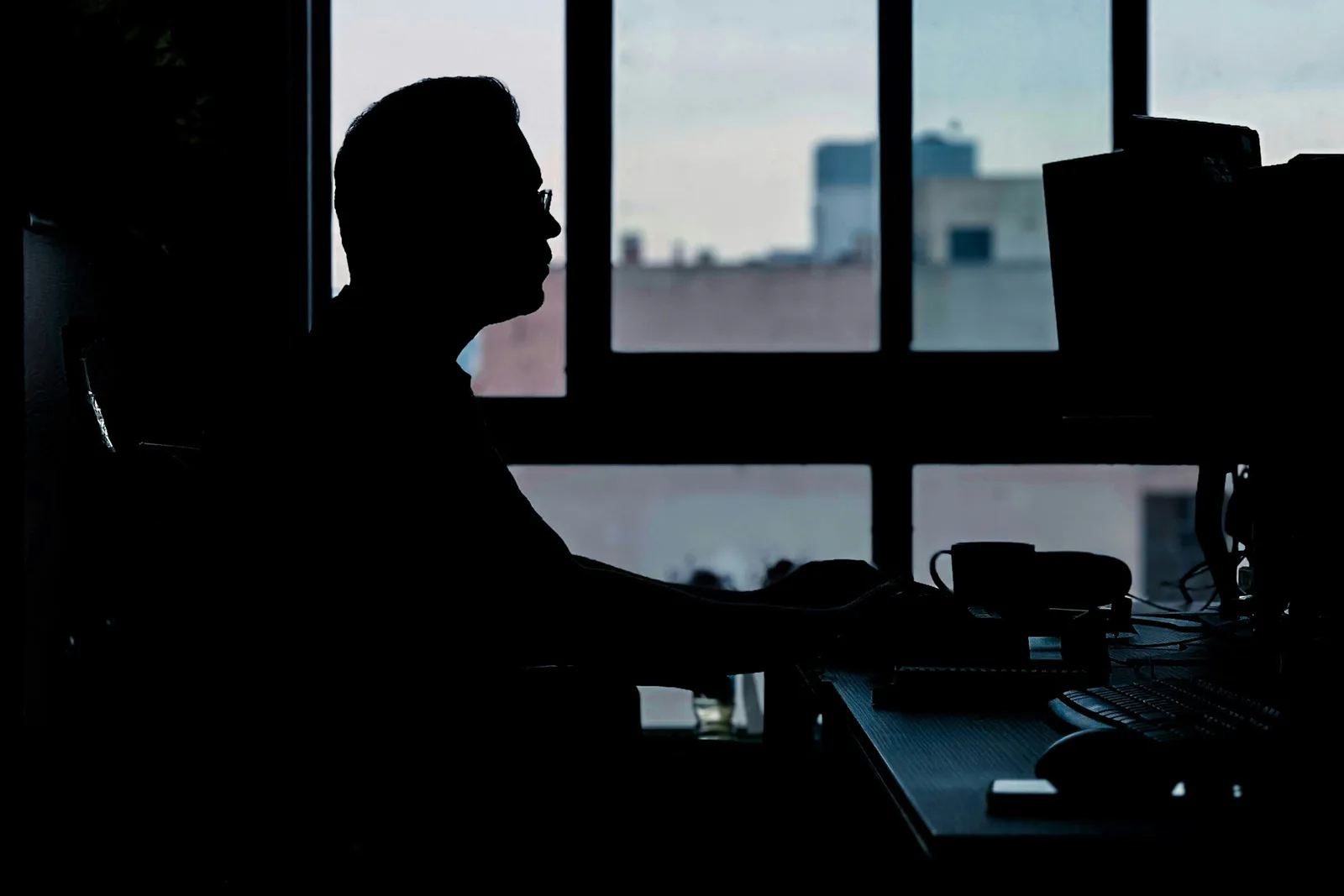 A person silhouetted at a desk beside an office window, their expression not visible