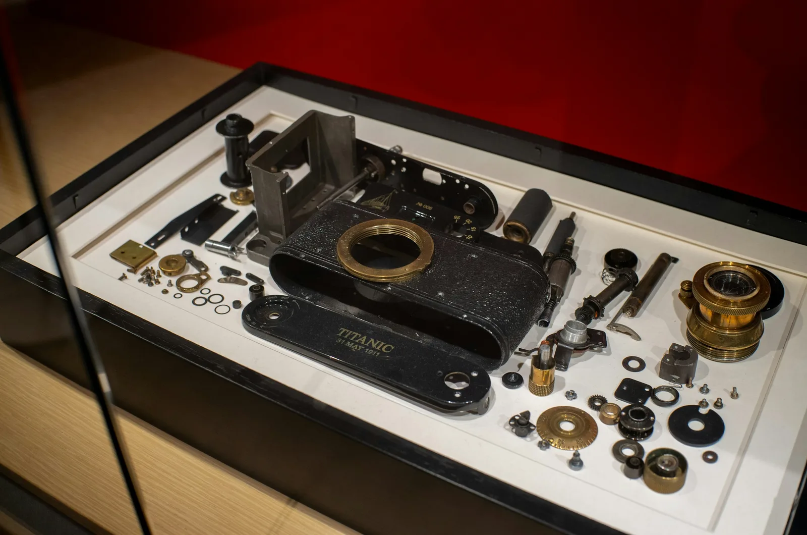 A vintage camera taken apart and laid out in a display case, every gear, screw, lens, and plate arranged beside the body it came from