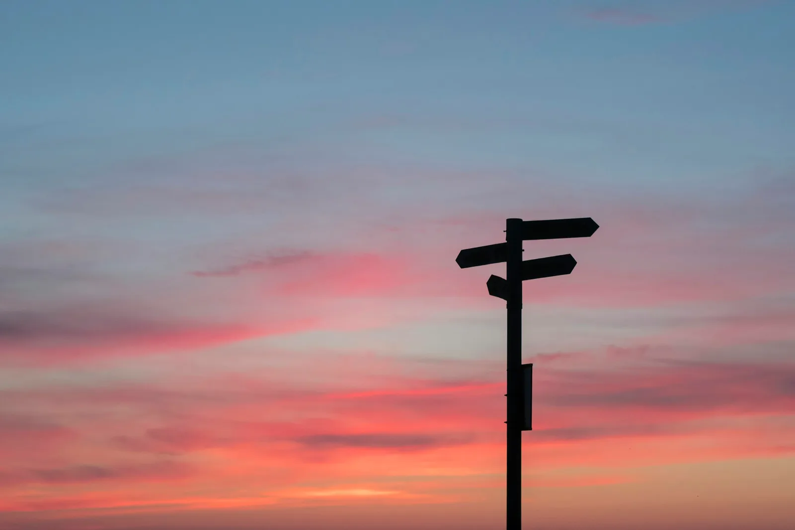 A signpost with arrows pointing in several directions, silhouetted against a sunset sky