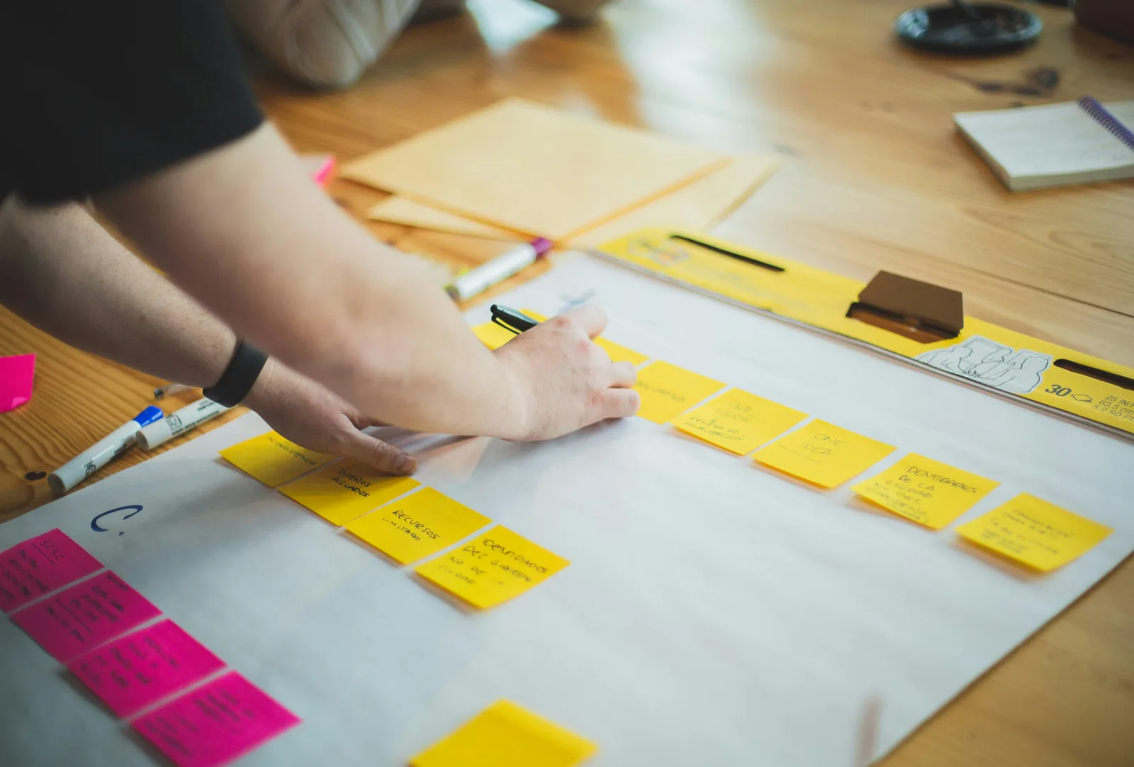 A person laying out task cards in sequence across a large sheet of paper, breaking a project into the individual pieces of work it contains