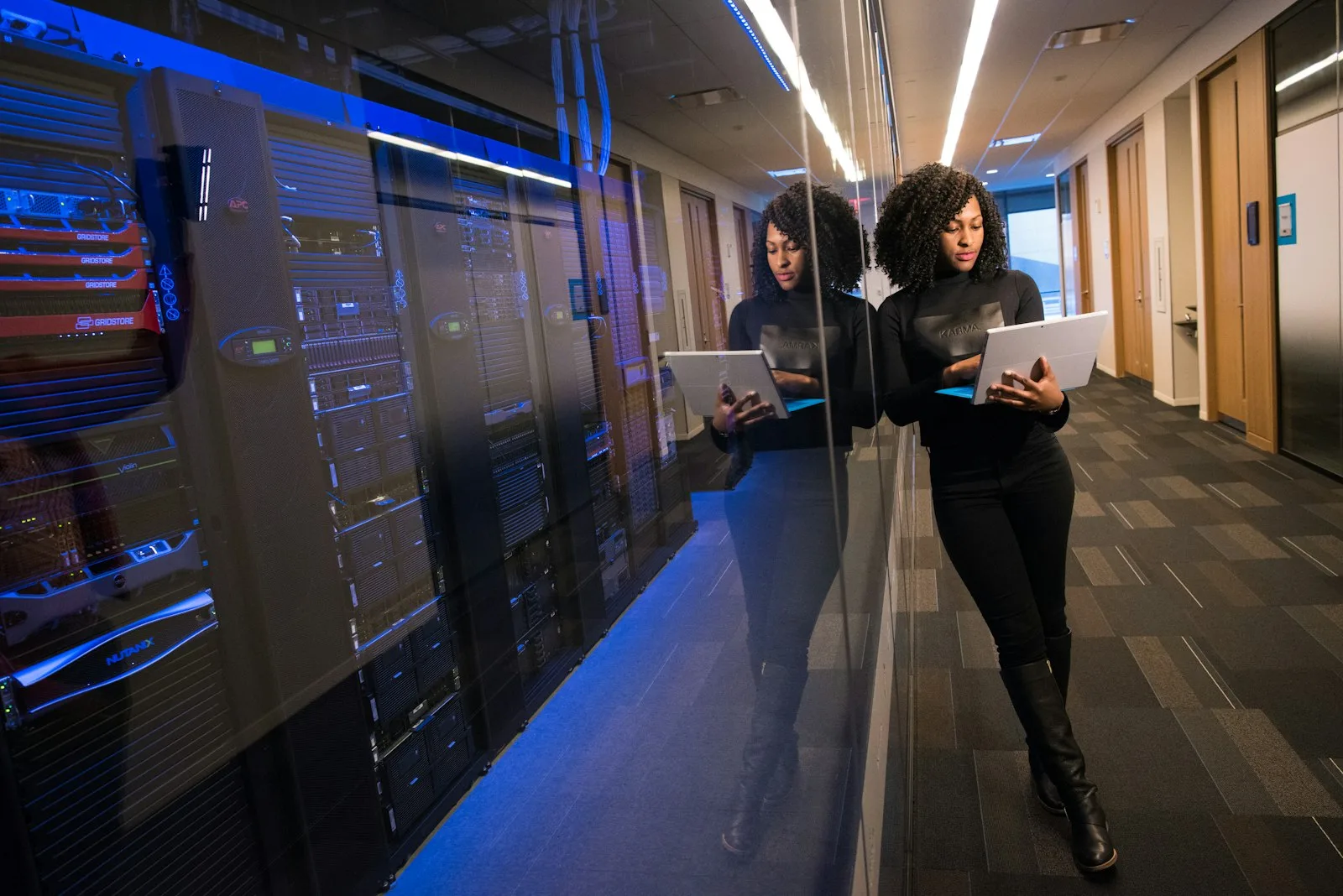 A woman holding a laptop beside server racks in a data center