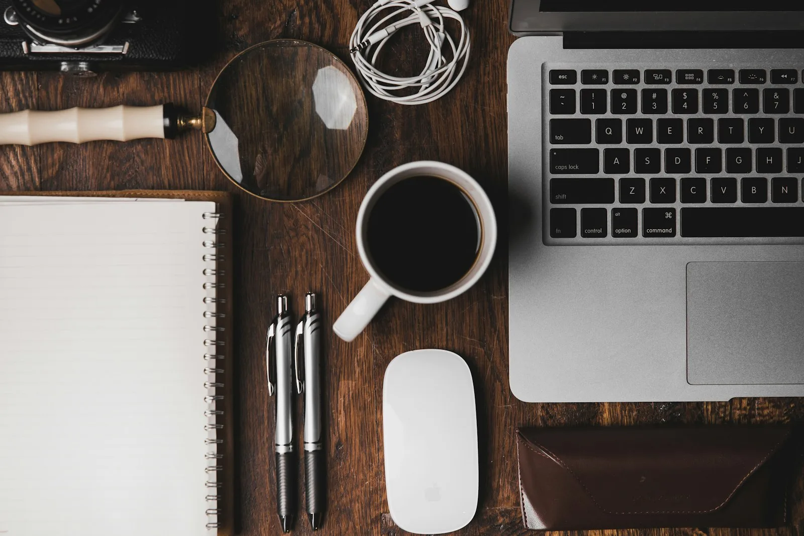 Overhead view of a notebook, pen, magnifying glass, and laptop on a desk